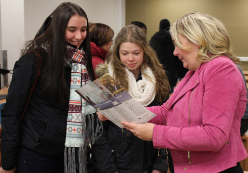 Deux jeunes femmes regardent une brochure présentée par une femme