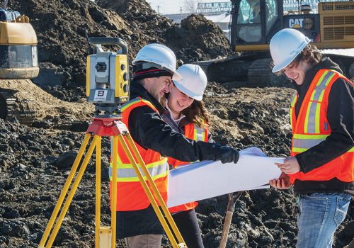 Trois étudiants en Génie civil sur un chantier au milieu de tas de terre et de pelles mécaniques