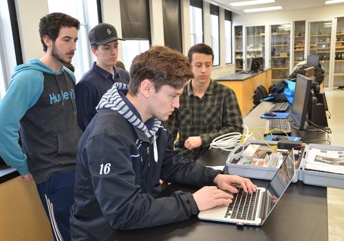 Trois étudiants observent un étudiant travaillant sur son ordinateur portable